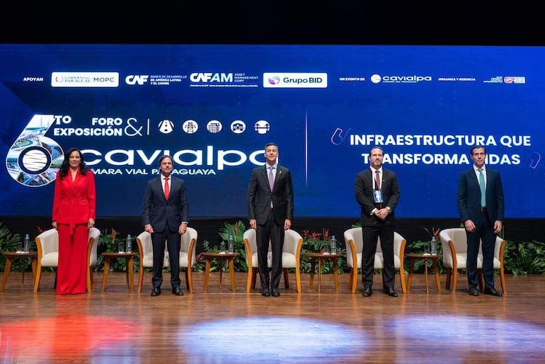 Santiago Peña en el podio con traje oscuro, acompañado por Claudia Centurión en traje rojo y otros funcionarios en un evento formal sobre infraestructura.