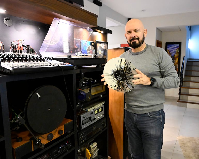 Jorge Puig sonríe sosteniendo un disco de vinilo en un moderno estudio musical, rodeado de equipos de sonido.