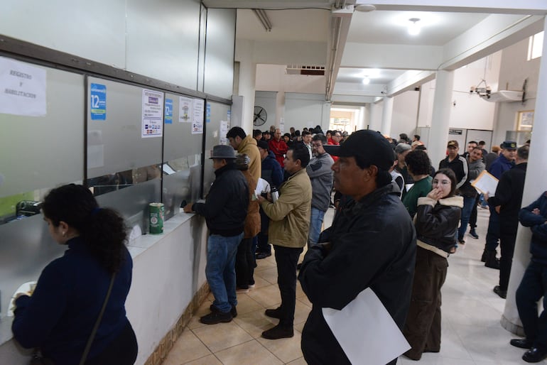Varias personas de pie en fila, sosteniendo documentos, en ambiente administrativo y organizado.