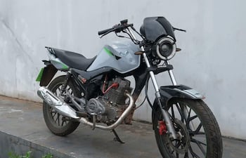 Motocicleta gris con detalles en negro y verde, estacionada sobre cemento en un ambiente exterior, sin personas presentes.