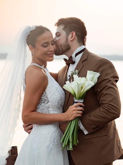 Pareja casándose al atardecer, la novia en vestido blanco y velo, el novio en traje marrón, mostrando complicidad y cariño.