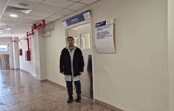 Hombre con abrigo negro en el Hospital General de Itapúa, frente a la puerta de urgencias, con expresión tranquila.