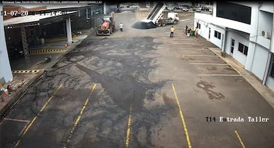 Cuatro hombres en un taller mecánico supervisan la descarga de asfalto desde un camión volquete en un ambiente exterior.