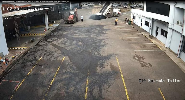 Cuatro hombres en un taller mecánico supervisan la descarga de asfalto desde un camión volquete en un ambiente exterior.