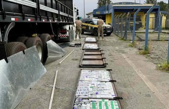 Tres agentes de seguridad en uniforme de camuflaje junto a un camión con cajas abiertas en un punto de control.