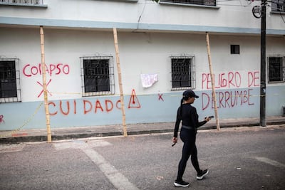 Una mujer pasa junto a un muro con una señal de advertencia de derrumbe después del terremoto de magnitud 7,4 que sacudió Pereira, Colombia.