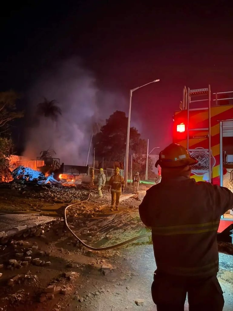 Cinco bomberos en uniforme luchan contra las llamas en un edificio dañado, mientras un bombero sostiene una manguera en primer plano.