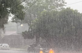 Dos vehículos, uno blanco y otro negro, parcialmente ocultos por la lluvia en una calle residencial de Ciudad del Este.