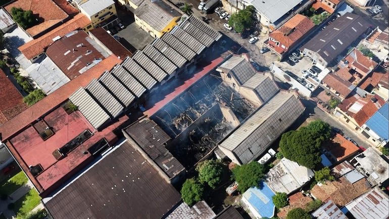 Edificio dañado por incendio, con humo y llamas visibles en escombros y áreas afectadas de un barrio urbano.