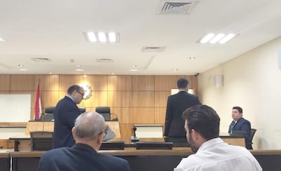 Un hombre de pie discute en la sala del tribunal mientras otros dos hombres observan en actitud neutral.