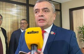 Carlos Liseras en traje azul y corbata roja, concentrado al hablar ante los medios, rodeado de otros hombres en un ambiente gubernamental.