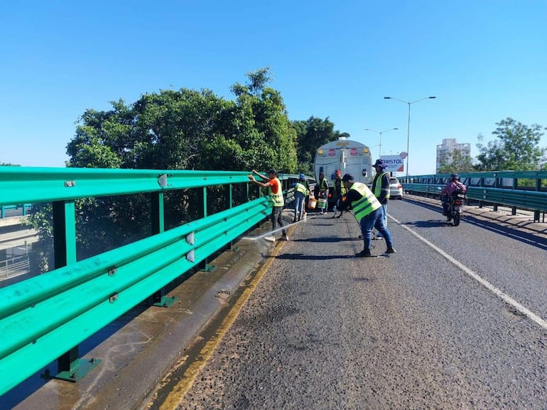 Trabajadores en chalecos de alta visibilidad llevan a cabo el mantenimiento del viaducto, con herramientas y vehículos visibles en el fondo.