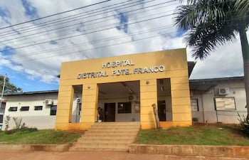 Fachada del Hospital Distrital de Presidente Franco, edificio amarillo con escaleras y nombre en letras metálicas plateadas, entorno con vegetación.