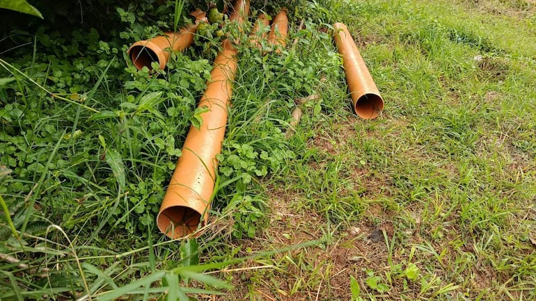 Varios tubos de plástico color naranja sobre hierba verde, dispersos en un área con vegetación, sin personas presentes.