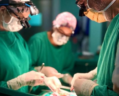 Cuatro profesionales médicos en quirófano, todos vestidos de verde, realizando una cirugía con instrumentos quirúrgicos.
