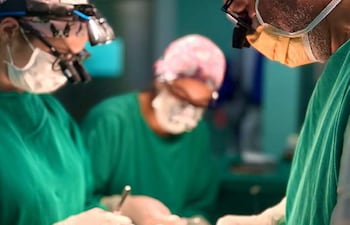 Cuatro profesionales médicos en quirófano, todos vestidos de verde, realizando una cirugía con instrumentos quirúrgicos.