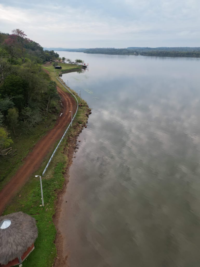 Muelle con banderas, mirador de palma y paisaje verde en un día nublado, sin personas a la vista.