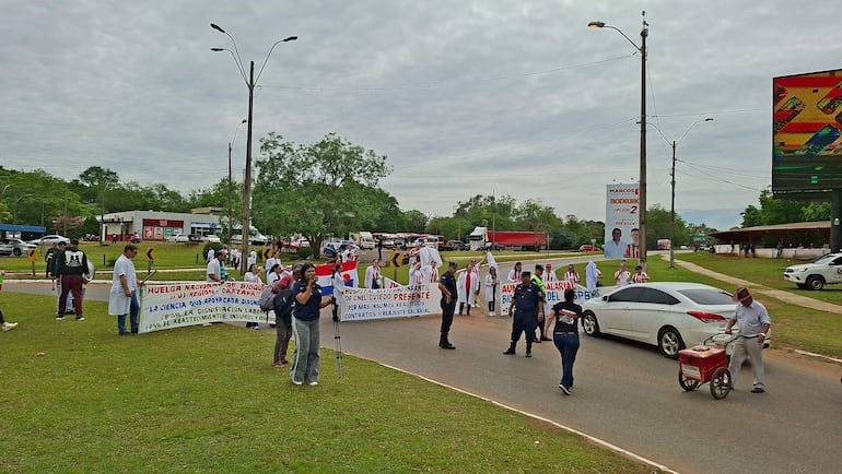 Manifestantes bioquímicos con camisetas blancas y carteles, mientras algunos agentes policiales observan la situación en la vía pública.