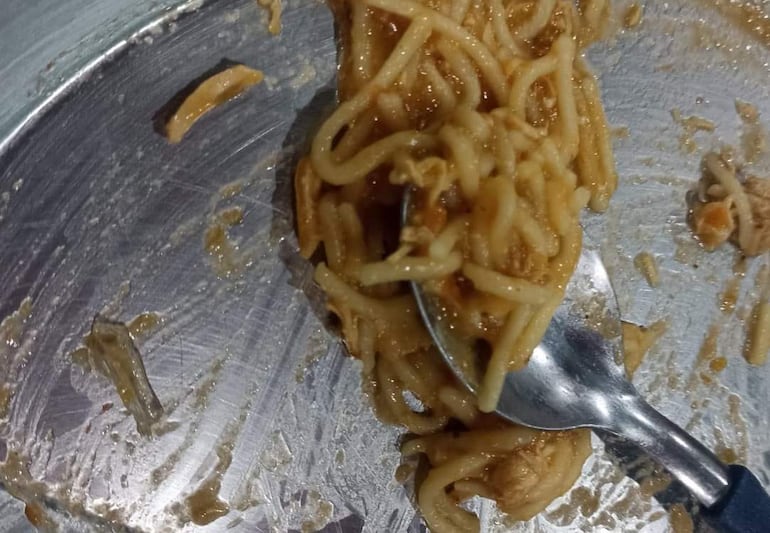 Un plato con fideos y carne en una mesa con mantel metálico refleja la luz, mostrando la comida parcialmente consumida.