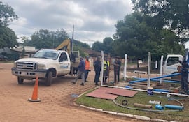 Siete trabajadores de ESSAP en ropa de trabajo y chalecos reflectantes, junto a camión y excavadora en obra de infraestructura.