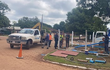 Siete trabajadores de ESSAP en ropa de trabajo y chalecos reflectantes, junto a camión y excavadora en obra de infraestructura.