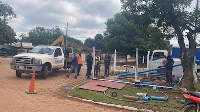 Siete trabajadores de ESSAP en ropa de trabajo y chalecos reflectantes, junto a camión y excavadora en obra de infraestructura.