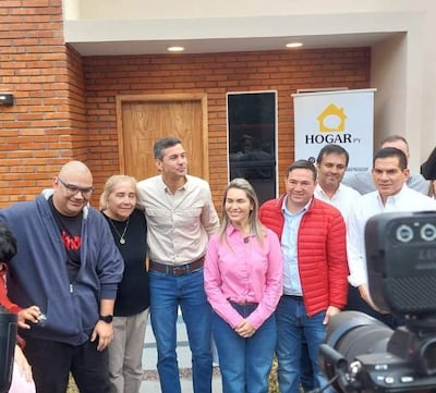 Manuel Aguilar con chaqueta roja, Santiago Peña en el centro y Johana Vega a su lado, todos sonrientes frente a un cartel de HOGAR.py.