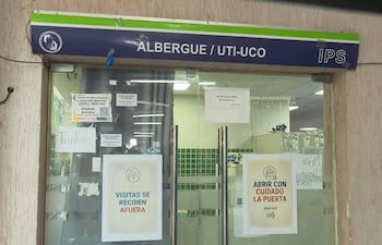 Entrada del albergue con puerta de vidrio y carteles informativos sobre visitas y contactos.