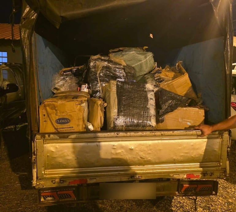 Parte trasera de un camión cargado con cajas y objetos envueltos, bajo escasa iluminación nocturna.