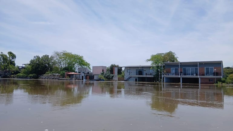 Edificios anegados por inundación, con reflejos en el agua y árboles alrededor en un paisaje exterior.