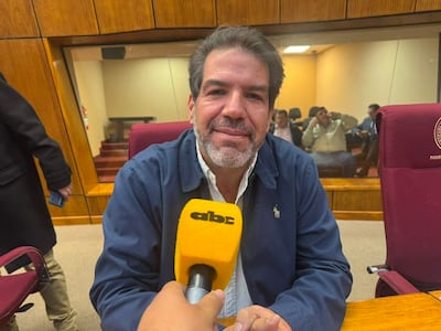 Rodrigo Blanco con chaqueta azul y camisa blanca, sonriendo frente a un micrófono amarillo, en un entorno formal.