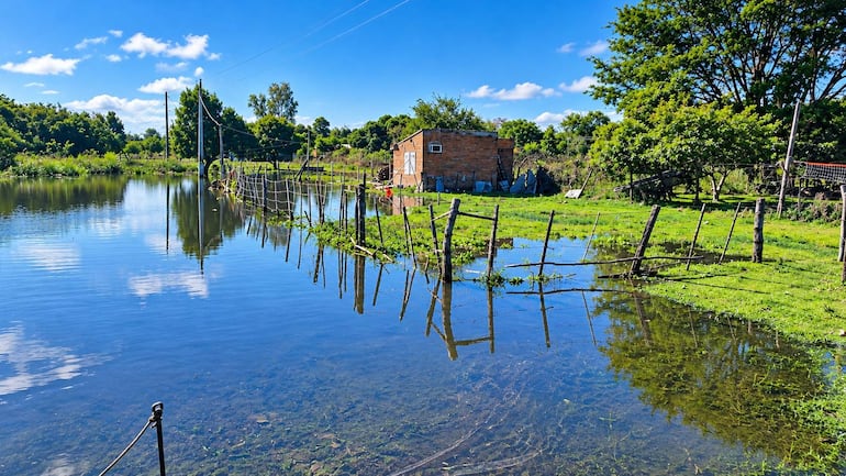 Paisaje rural con casa de ladrillos y vegetación densa rodeada de agua clara bajo un cielo despejado.