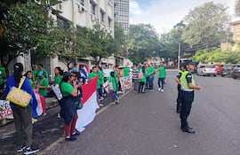 Grupo de personas en camisetas verdes sosteniendo banderas en una manifestación, con oficiales de policía presentes en el entorno urbano.