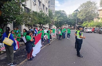 Grupo de personas en camisetas verdes sosteniendo banderas en una manifestación, con oficiales de policía presentes en el entorno urbano.