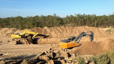 Dos excavadoras amarilla y naranja operan en terreno removido, rodeadas de árboles y tierra acumulada.