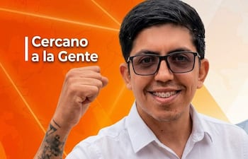 Christian Flores, con camisa blanca y gafas, sonríe y levanta el puño en un fondo naranja con su nombre y lema publicitario.