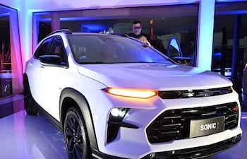 El SUV Chevrolet Sonic en primer plano, iluminado con luces azules y rosas, mientras dos personas exploran el vehículo.