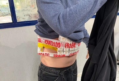 Persona con prenda azul y pantalones oscuros sostiene un objeto negro, con paquetes etiquetados como 'frágil'.