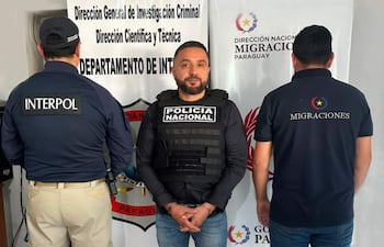 Hombres en chalecos de policía y migraciones en conferencia, con carteles de instituciones visibles en el fondo.