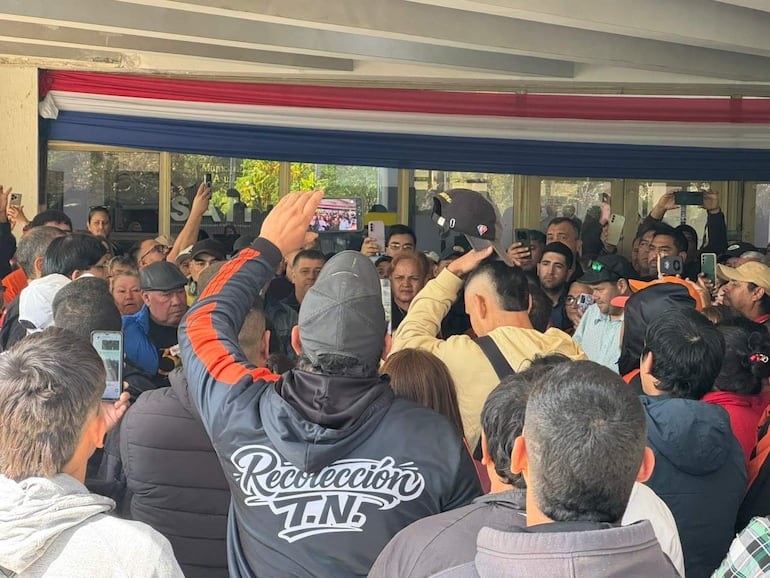 Grupo de funcionarios en Asunción con camisetas oscuras y chaquetas, sosteniendo teléfonos y un banner con los colores paraguayos.