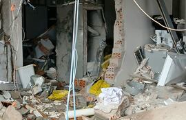 Espacio interior desordenado con escombros, materiales de construcción y objetos como un bote de basura blanco y una bolsa amarilla.