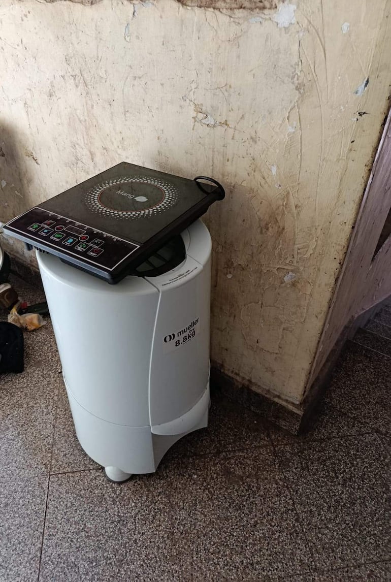 Un lavador Mueller de 8.8 kg y una cocina eléctrica de inducción en un ambiente interior desgastado.