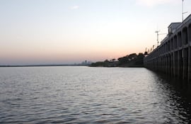 Vista serena del río Paraguay, con un muelle a la izquierda y vegetación a la derecha, bajo un cielo con suaves colores de atardecer.