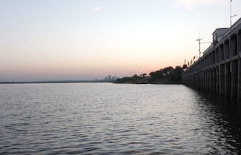Vista serena del río Paraguay, con un muelle a la izquierda y vegetación a la derecha, bajo un cielo con suaves colores de atardecer.