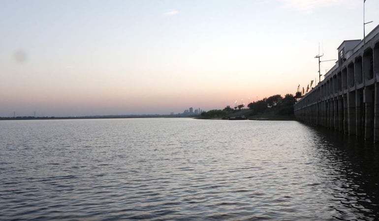 Vista serena del río Paraguay, con un muelle a la izquierda y vegetación a la derecha, bajo un cielo con suaves colores de atardecer.