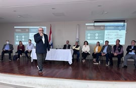 Isaías Ricardo Fretes presenta en la mesa mientras Enrique Duarte Luraghi y Vanessa Cubas lo observan, en un ambiente formal.