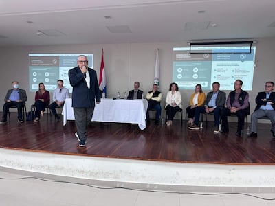Isaías Ricardo Fretes presenta en la mesa mientras Enrique Duarte Luraghi y Vanessa Cubas lo observan, en un ambiente formal.