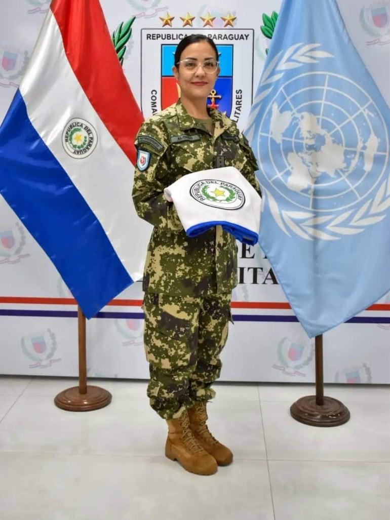 María Eugenia Alonso Iglesias en uniforme militar, sosteniendo camiseta de Paraguay, con banderas de Paraguay y ONU en el fondo.