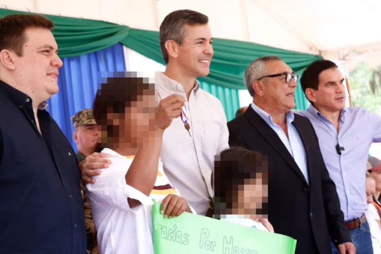 Cesarito Sosa sonriente con abrigo oscuro, Juan Carlos Baruja y Santiago Peña felices en un evento al aire libre con decoración verde y azul.