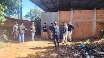 Grupo de seis hombres, algunos en chaquetas oscuras, conversando en un entorno desordenado y al aire libre.